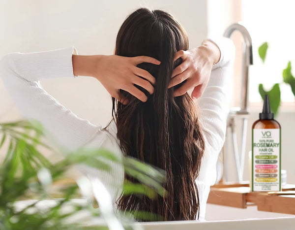 Person washing hair in a sink with a bottle of rosemary hair oil in the background